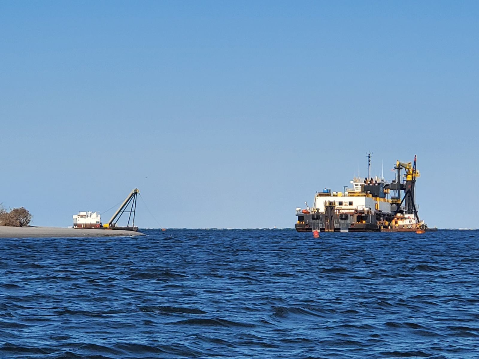 A dredge and a pipeline crane working the water off the south end of Masonboro Island, April 2026